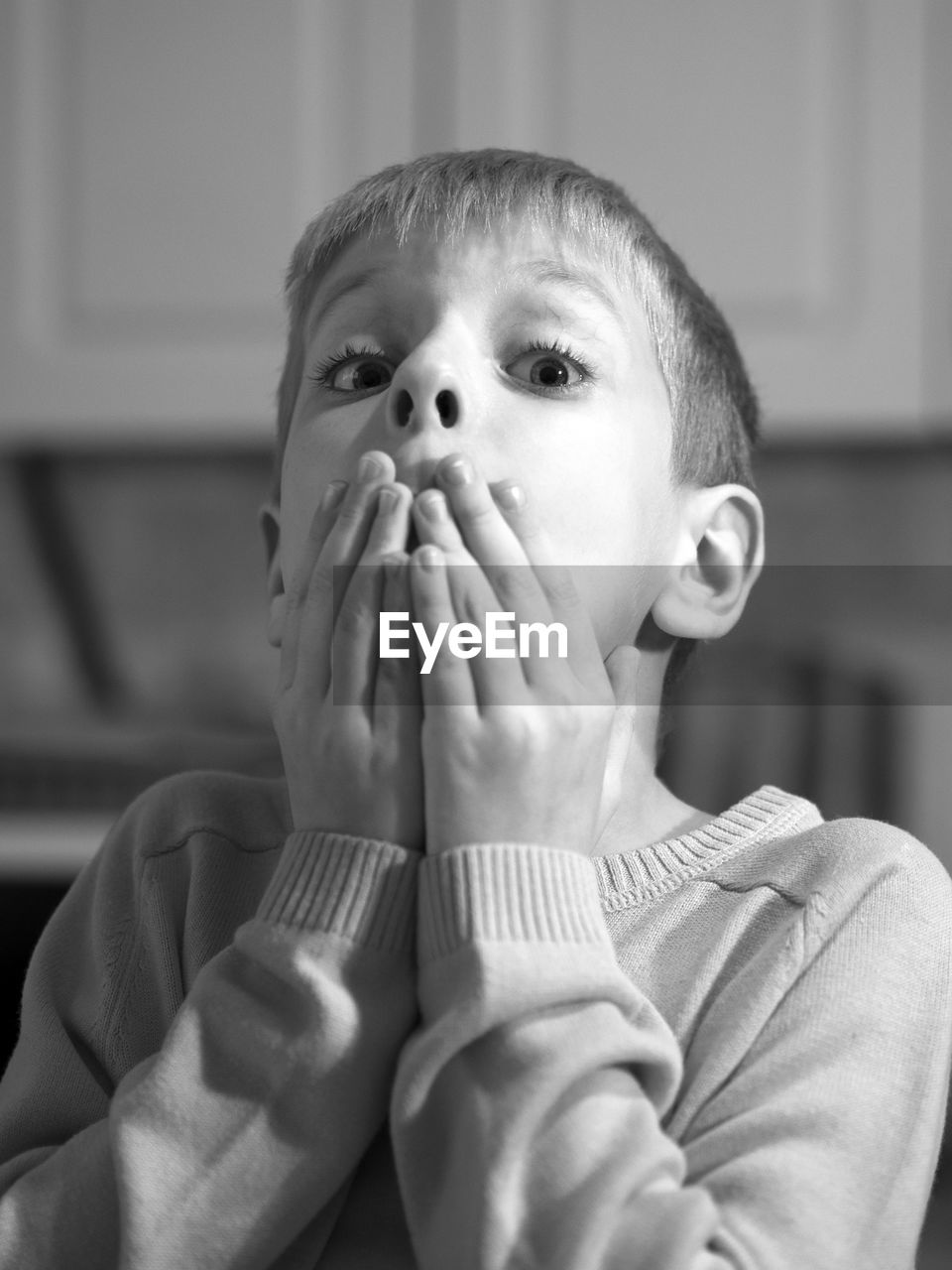 Close-up portrait of shocked boy covering mouth at home