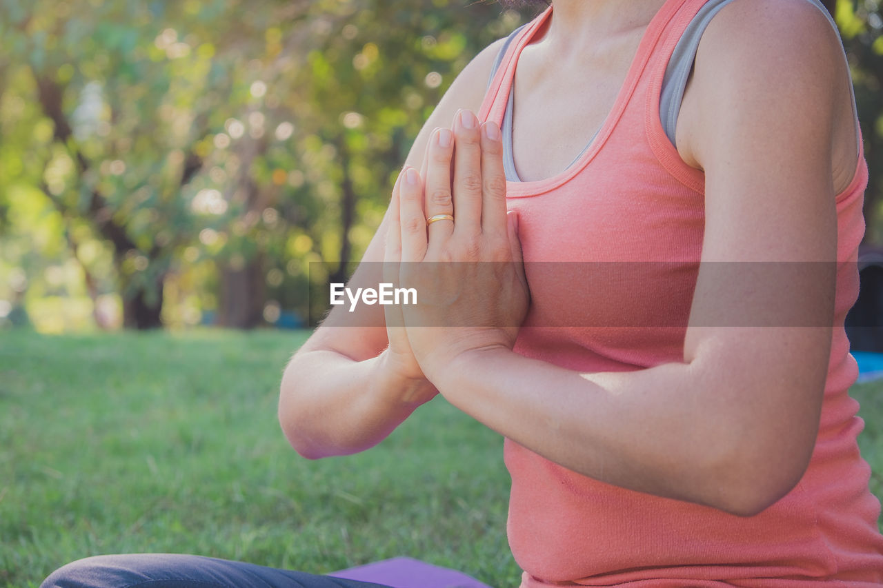 MIDSECTION OF WOMAN SITTING BY GRASS