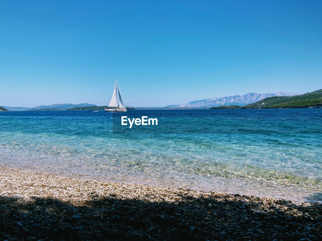 Sailboat sailing in sea against clear blue sky