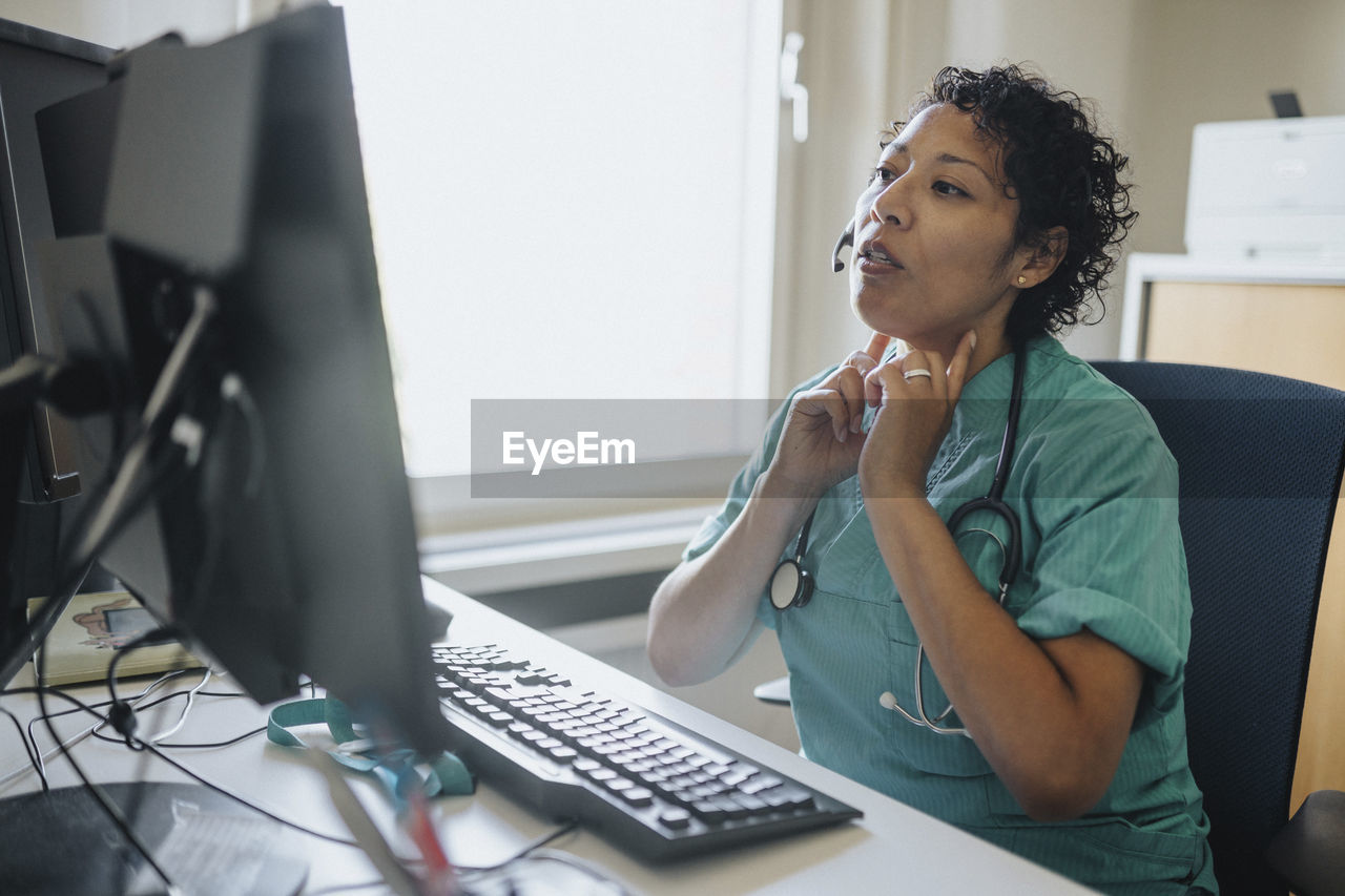 Female doctor giving advice through video call while sitting at desk in hospital