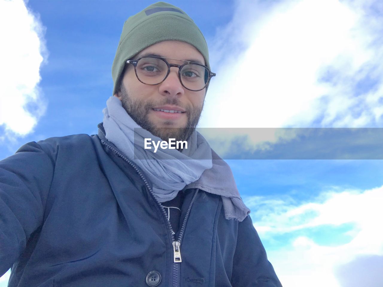 Self portrait of smiling young man wearing knit hat against sky