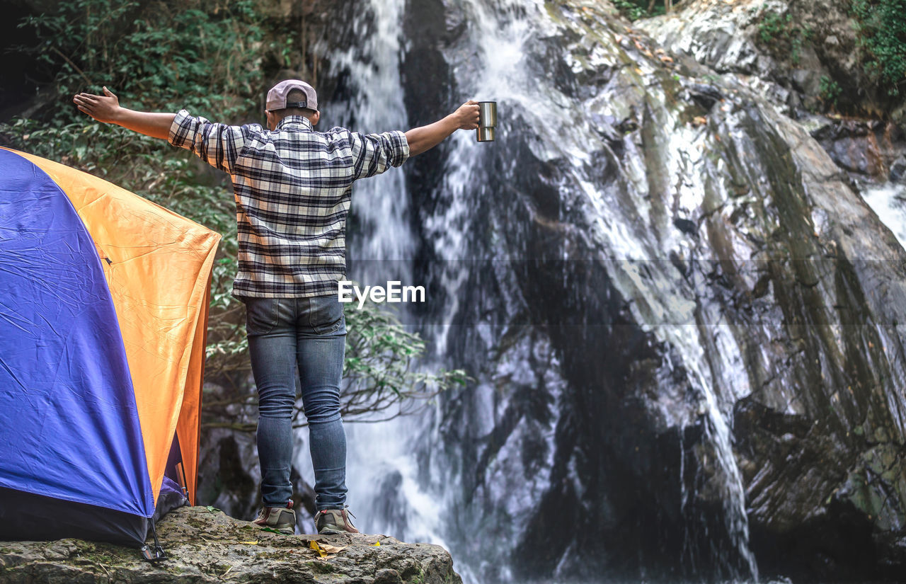 Happy male tourist standing and drinking coffee at the waterfall