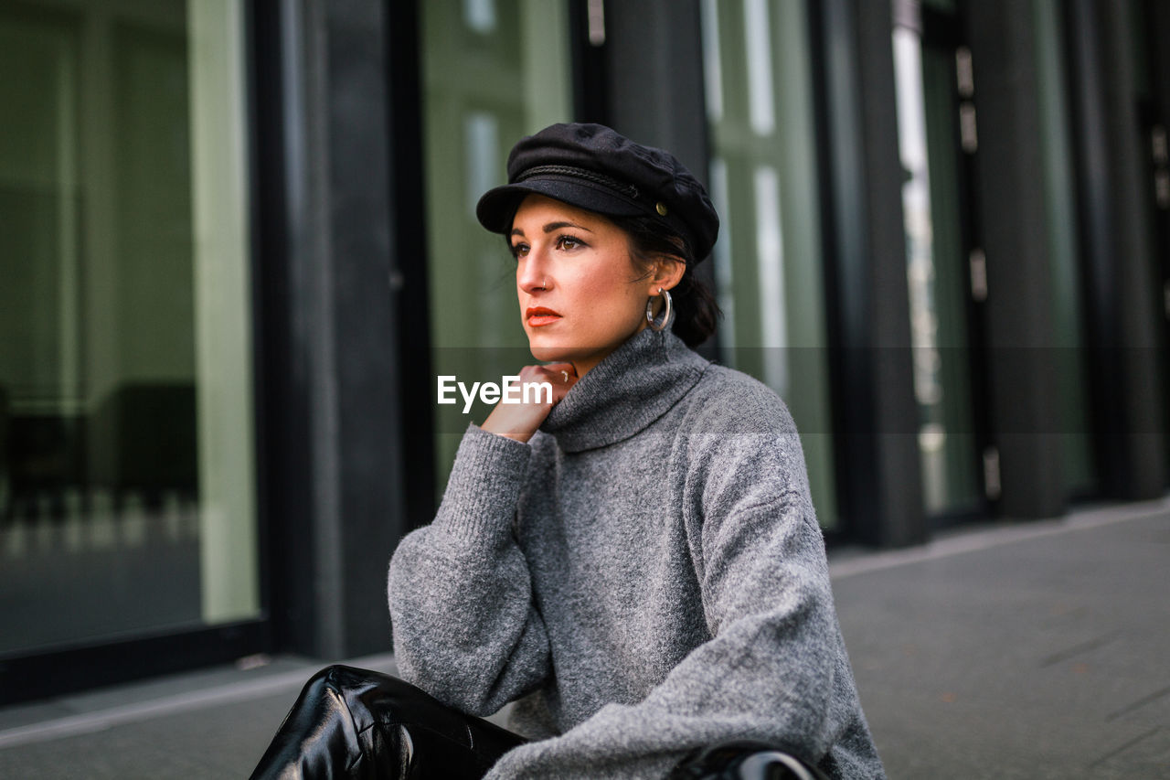 PORTRAIT OF YOUNG WOMAN LOOKING AWAY WHILE SITTING ON GREEN WALL