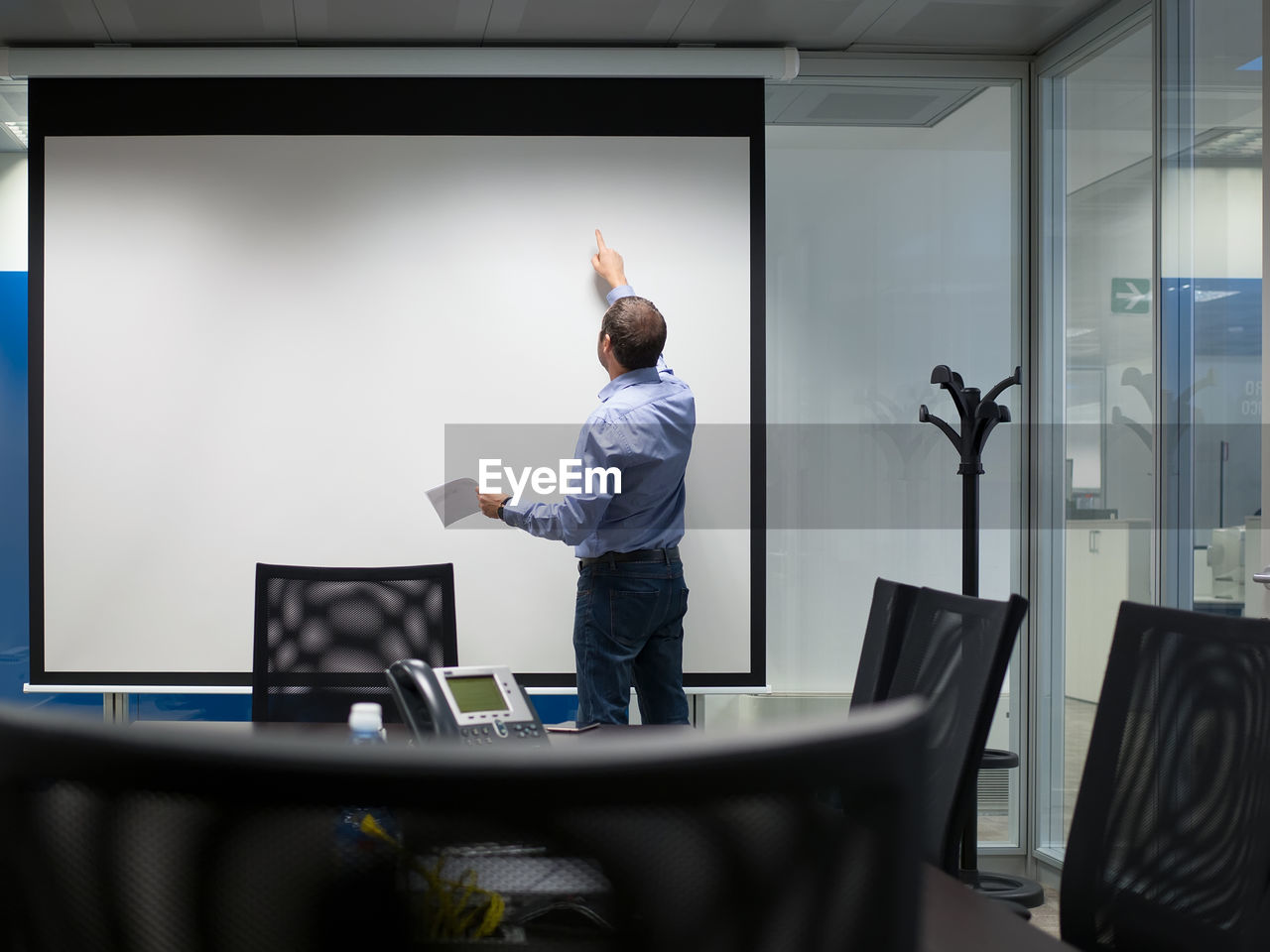 Rear view of businessman standing by projection screen in board room at office