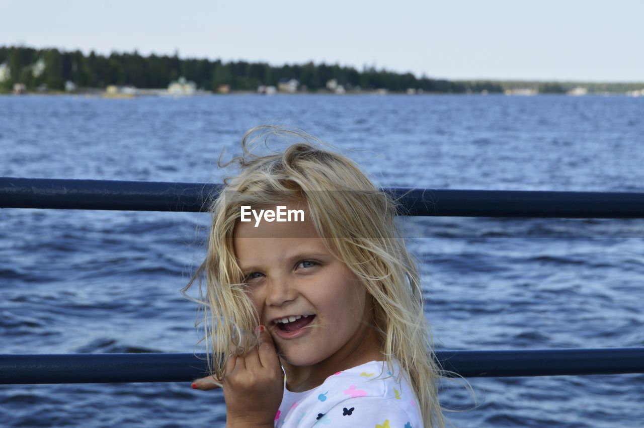 Portrait of cheerful girl standing by railing against sea