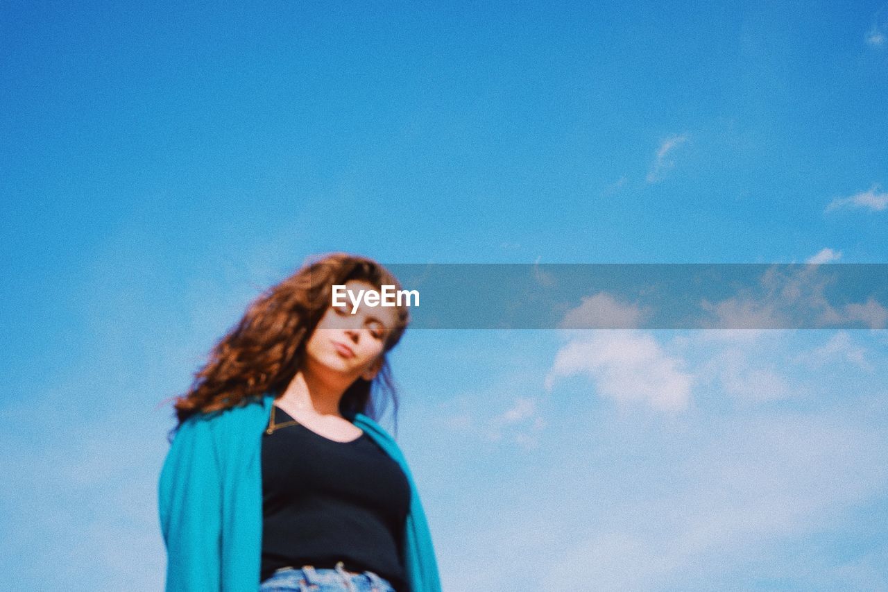 LOW ANGLE VIEW OF YOUNG WOMAN STANDING AGAINST SKY