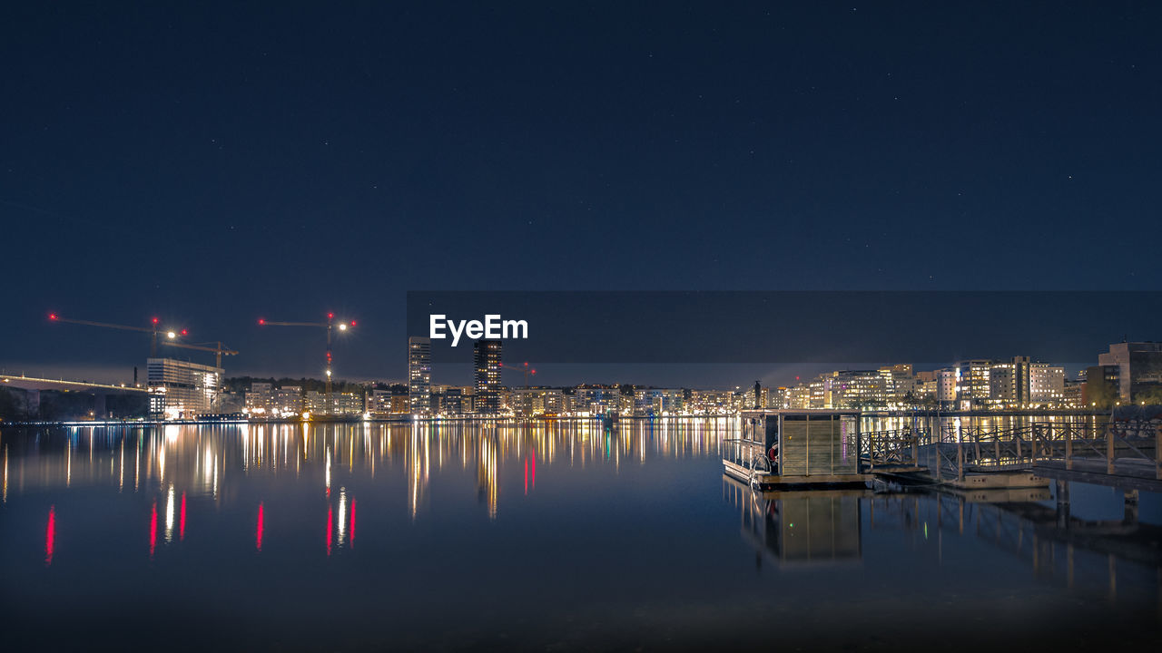 Boats moored in illuminated city against sky at night