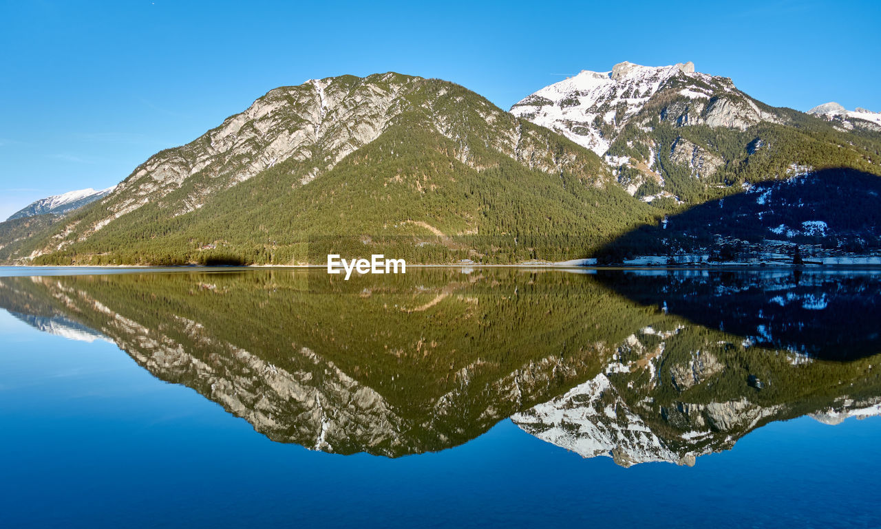 Scenic view of lake by mountains against clear blue sky