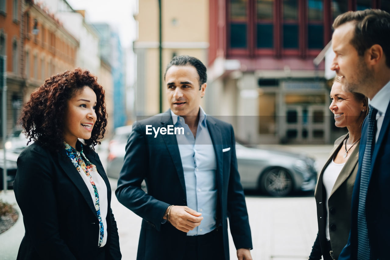 Smiling business colleagues talking while standing in city