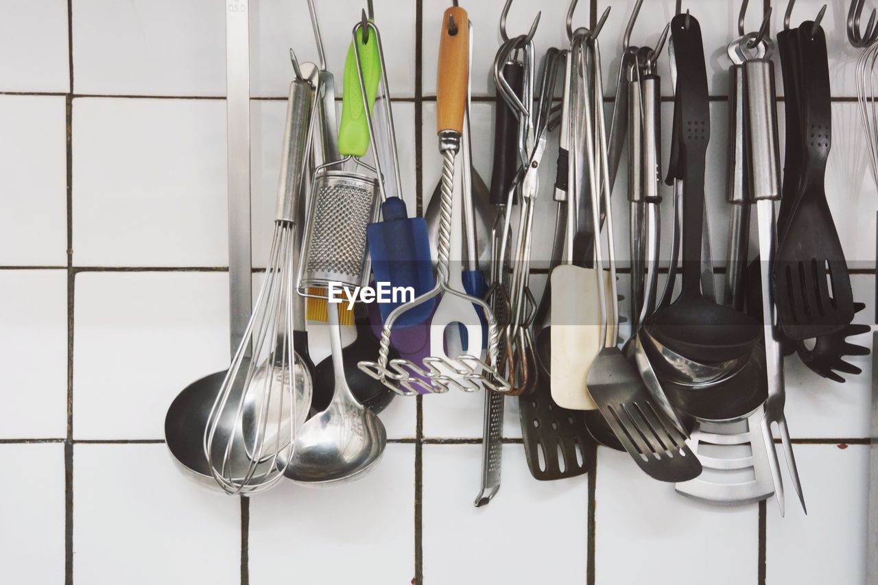 Close-up of spoons and spatulas hanging against wall in kitchen