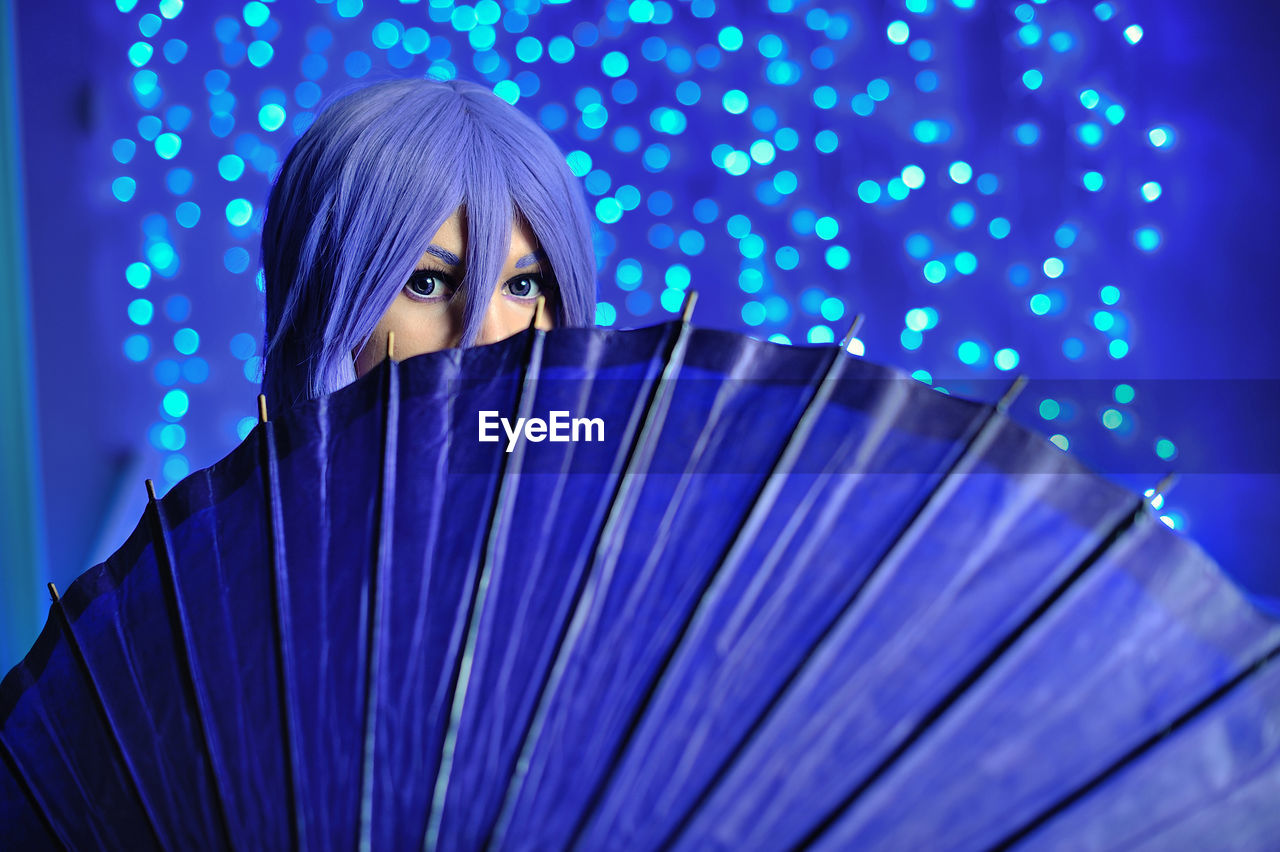 Portrait of woman holding purple umbrella while standing against defocused lights