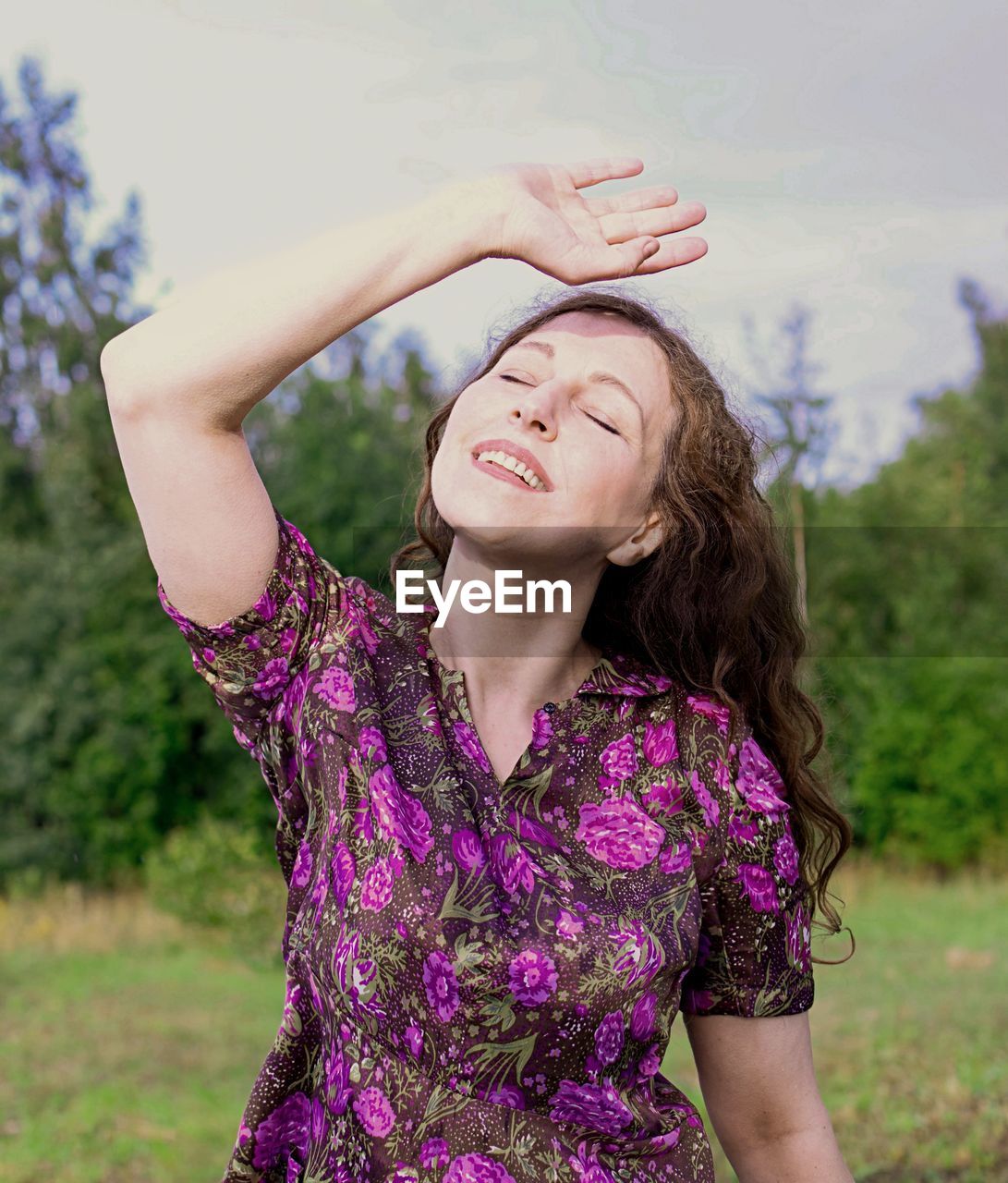 Smiling woman shielding eyes while standing outdoors