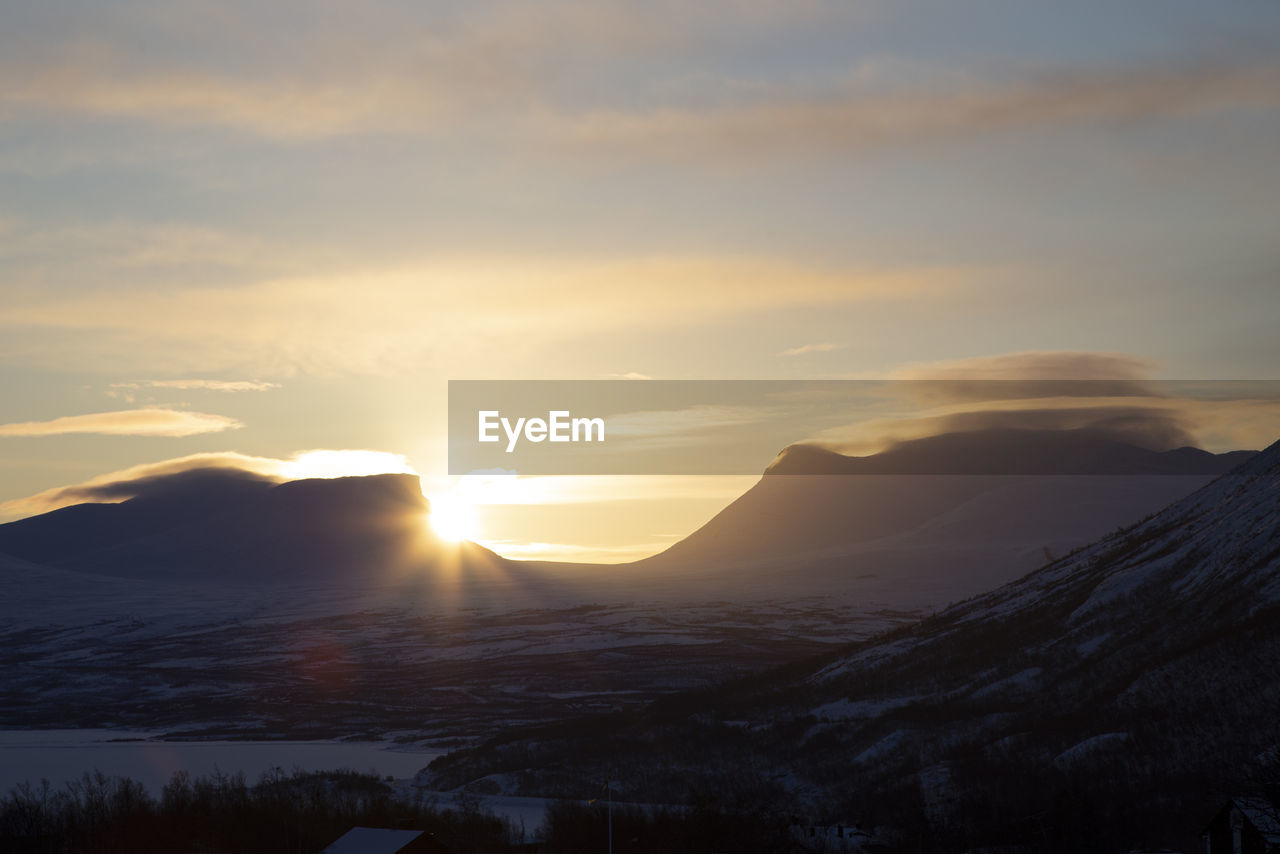 sky, mountain, beauty in nature, scenics - nature, environment, sunrise, cloud, landscape, dawn, nature, tranquility, morning, mountain range, sun, tranquil scene, sunlight, no people, sunbeam, snow, non-urban scene, cold temperature, idyllic, winter, silhouette, land, dramatic sky, outdoors, travel destinations, travel, lens flare, horizon, remote, back lit, tourism, tree