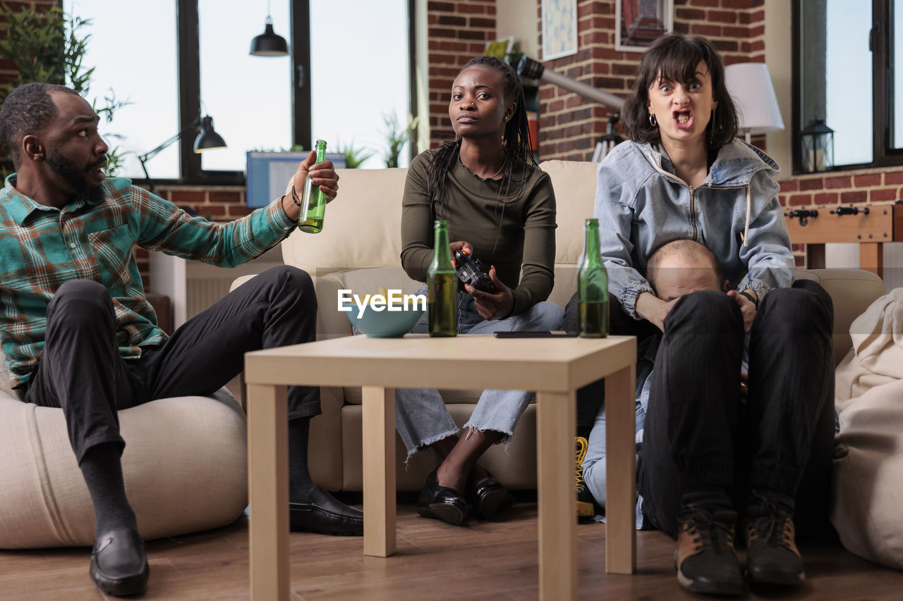 smiling friends using mobile phone while sitting on table at home