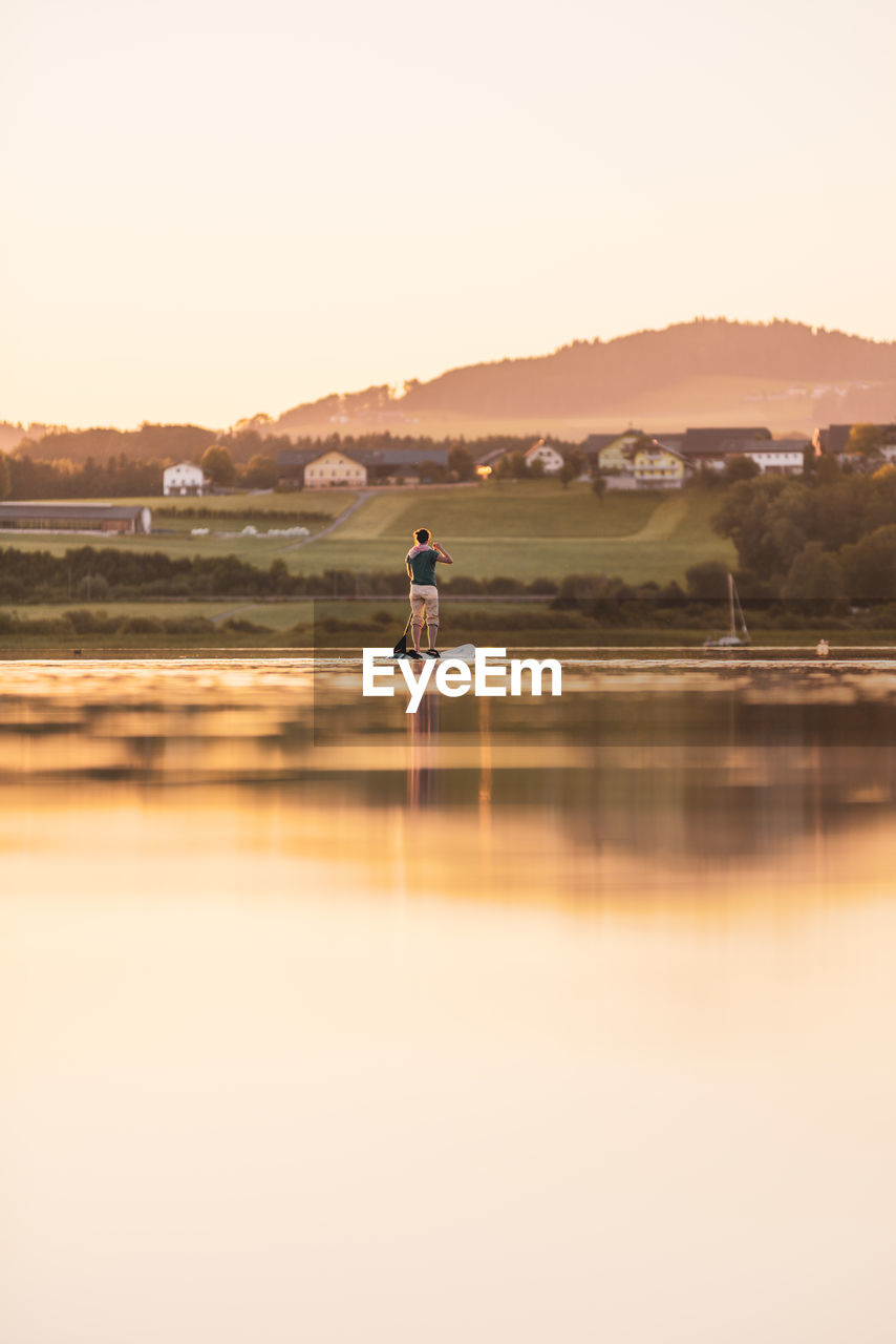 Young woman stand up paddling at sunset, lake wallersee, austria