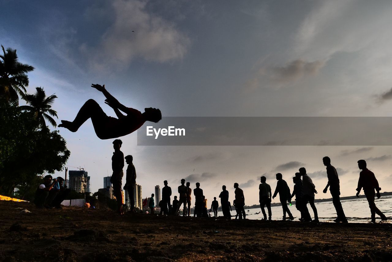 SILHOUETTE OF PEOPLE JUMPING AGAINST SKY DURING SUNSET