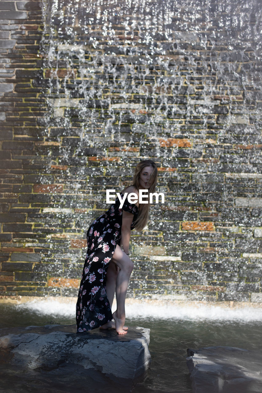 FULL LENGTH SIDE VIEW OF WOMAN WITH ARMS RAISED AGAINST WATER