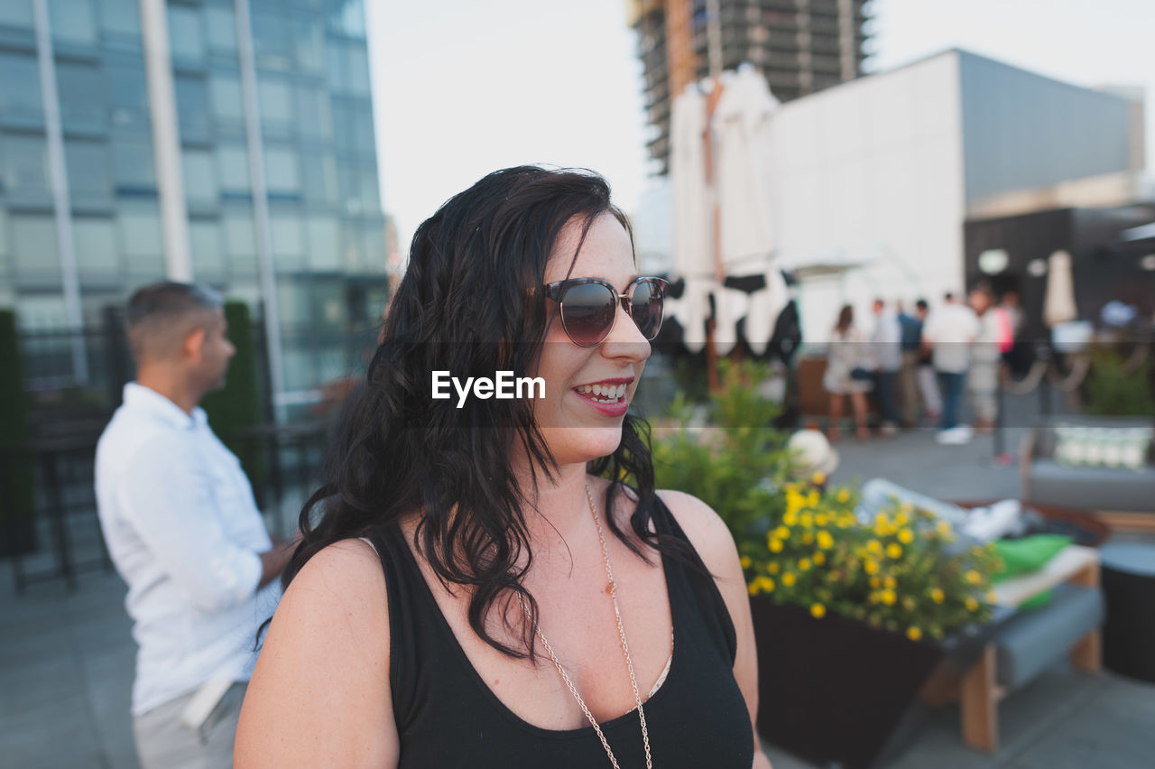 Smiling young woman wearing sunglasses while looking away in city