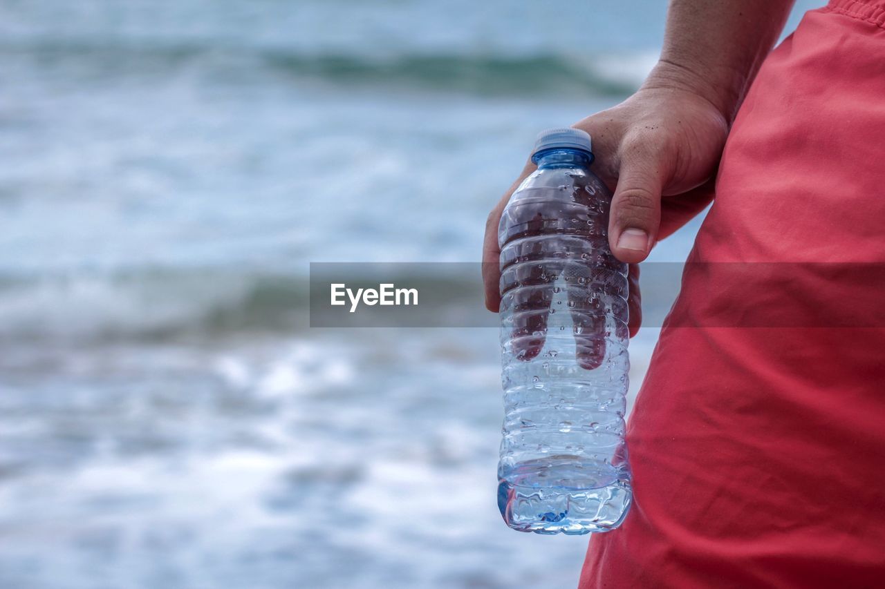 Close-up of man holding plastic bottle against sea