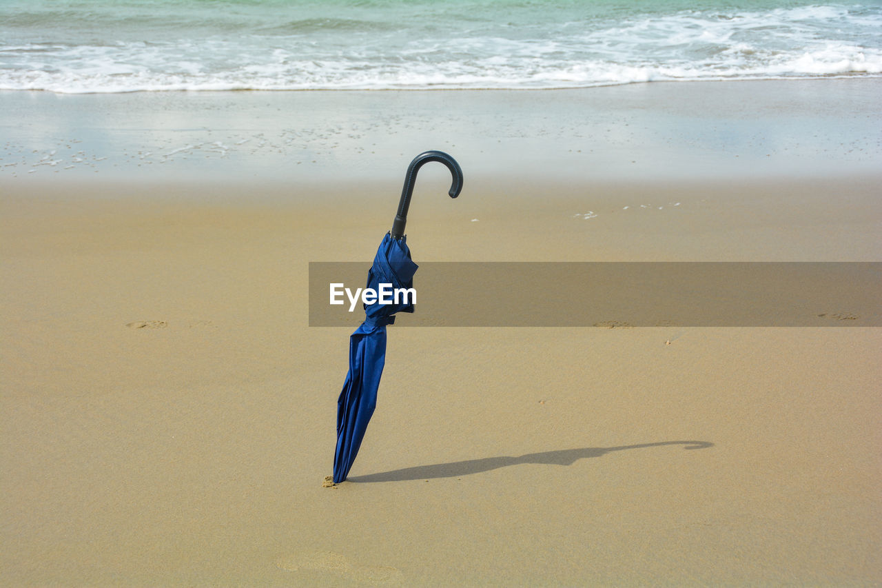 A closed umbrella is stuck in the sand, on the beach in the sunlight