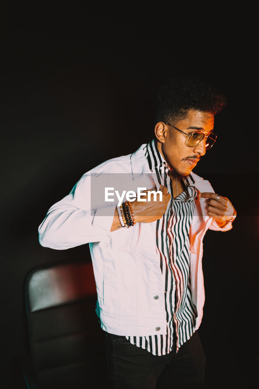 Young african american masculine male wearing stylish clothes and sunglasses with bracelets adjusting jacket