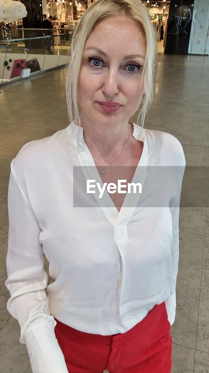 looking at camera, portrait, adult, one person, women, blond hair, front view, clothing, female, mature adult, smiling, waist up, person, standing, business, indoors, blouse, emotion, human face, lifestyles, fashion, three quarter length, white, hairstyle, businesswoman, human hair
