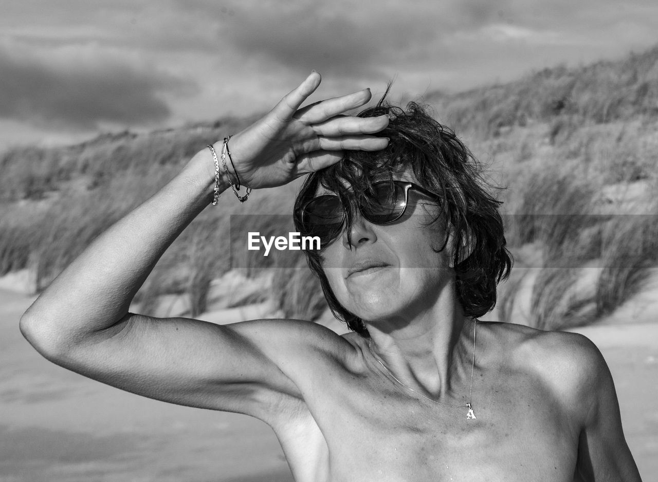 Shirtless woman wearing sunglasses shielding eyes at beach