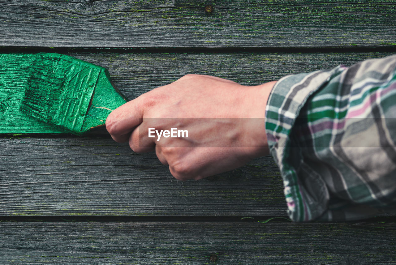 Female hand paints the weathered wooden wall of an old house with green paint, home redecoration