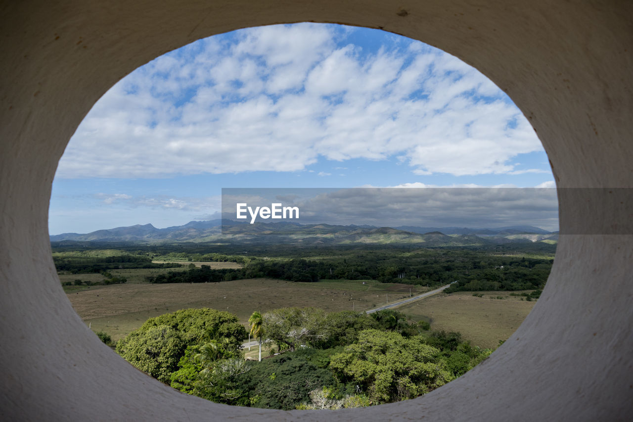 Scenic view of landscape against cloudy sky seen from circle window