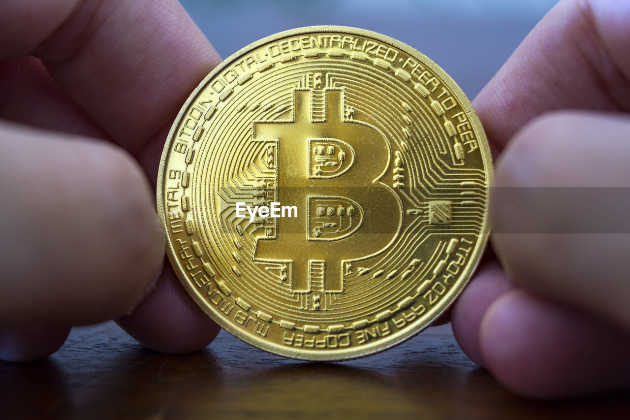 Close-up of cropped hands holding bitcoin on table
