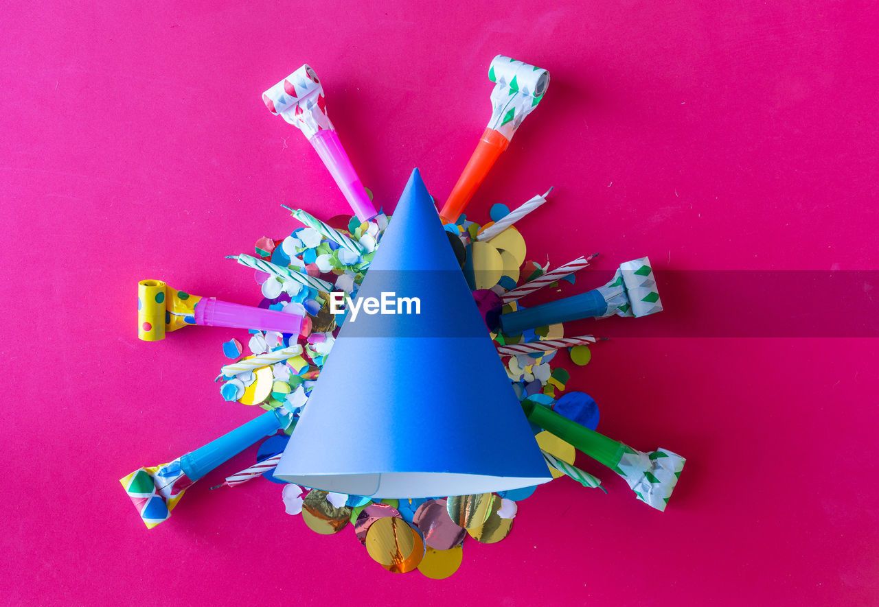 High angle view of multi colored confetti with party hat on pink background