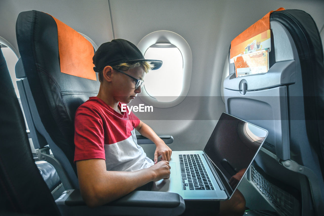 Side view of boy using laptop while sitting in airplane