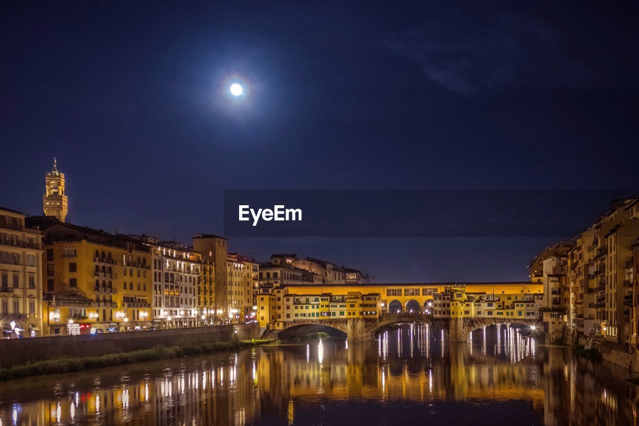 Illuminated arch bridge over river in city against sky at night