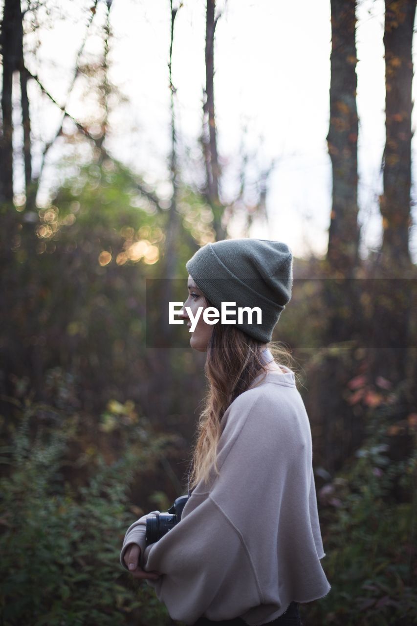 SIDE VIEW OF YOUNG WOMAN IN FOREST AGAINST TREES