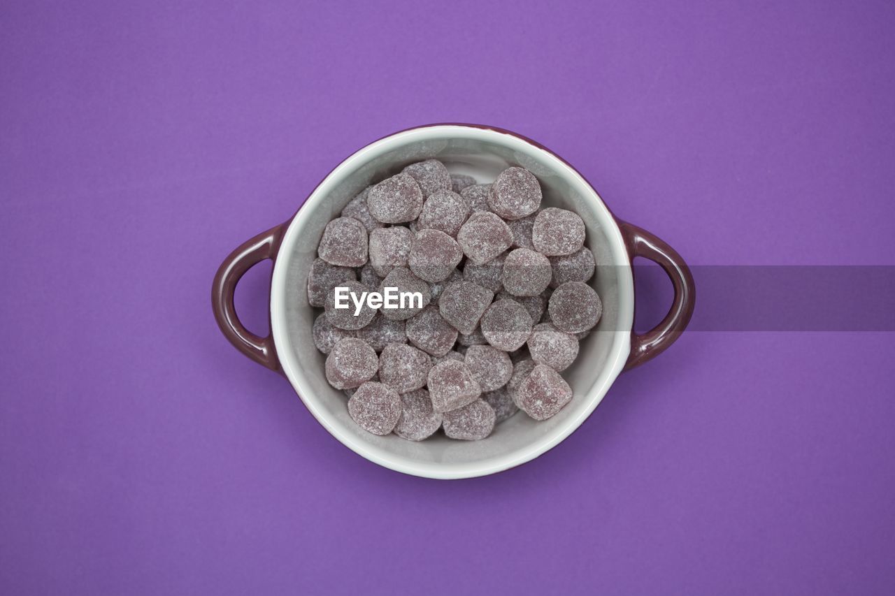Directly above view of candies in bowl on purple background