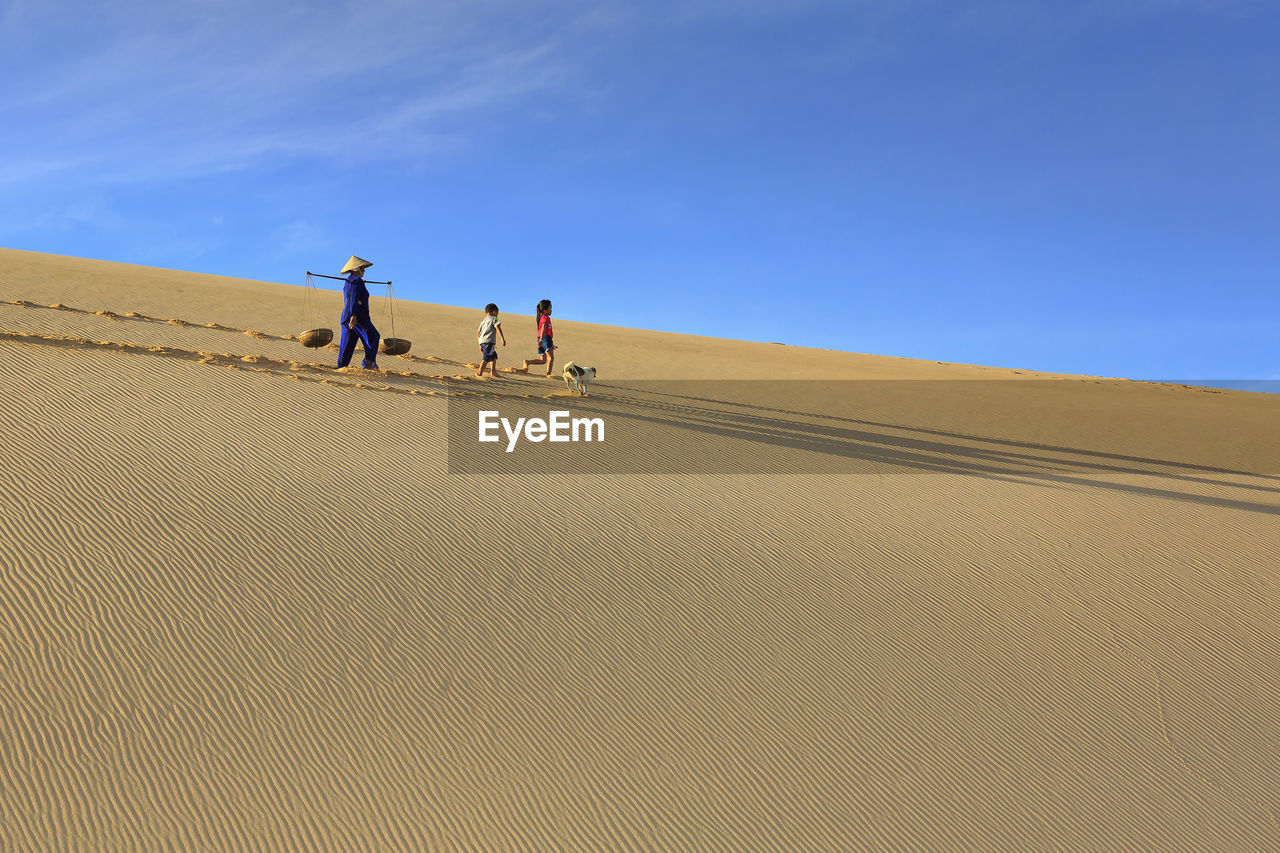 REAR VIEW OF MEN ON SAND DUNE IN DESERT