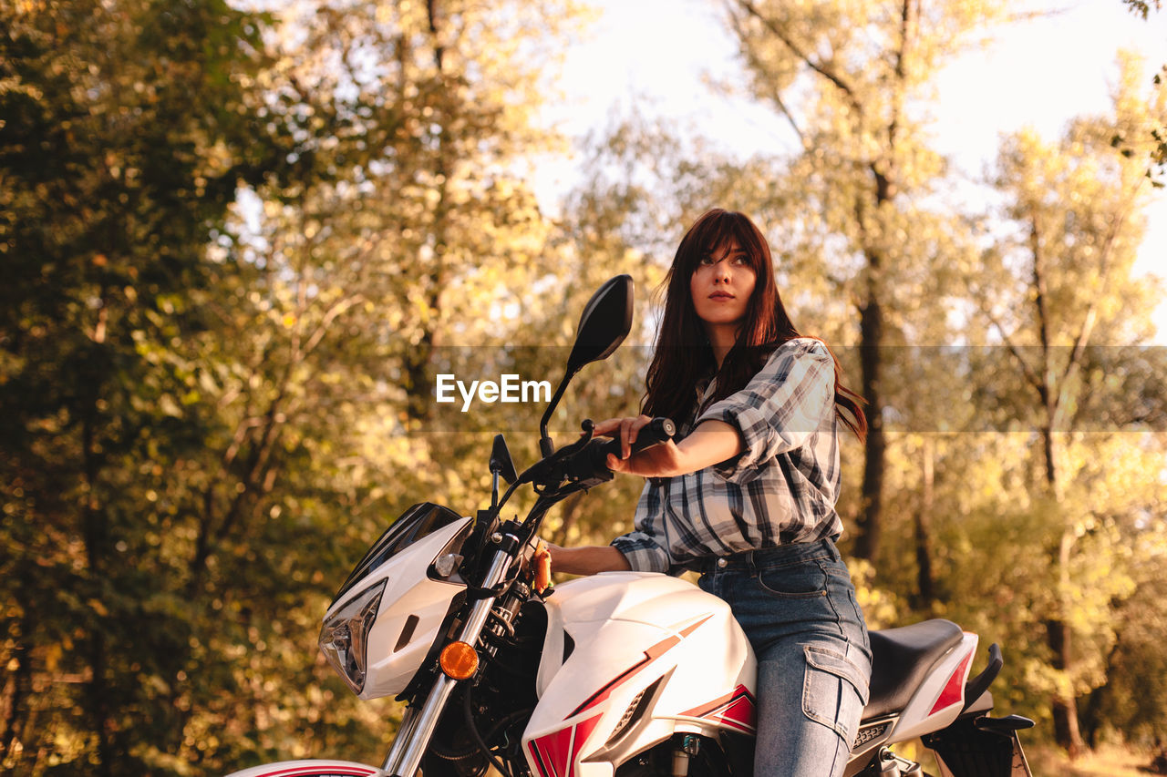 Confident young woman riding motorcycle amidst trees in forest