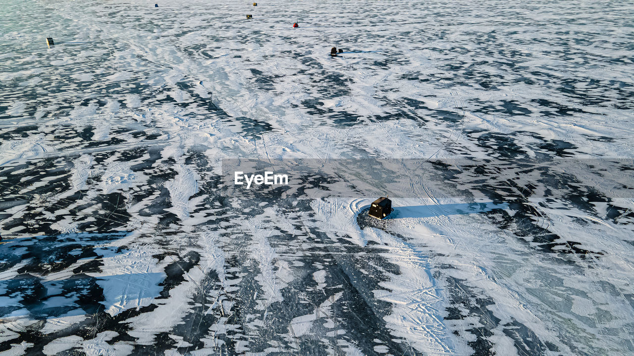 Aerial of frozen lake with patterns and fishing huts in the early morning