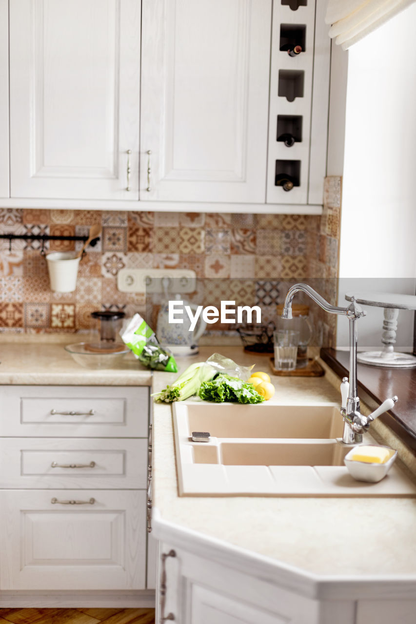 The vegetables are on the table next to the sink. kitchen faucet, sink, kitchen, vegetables. 