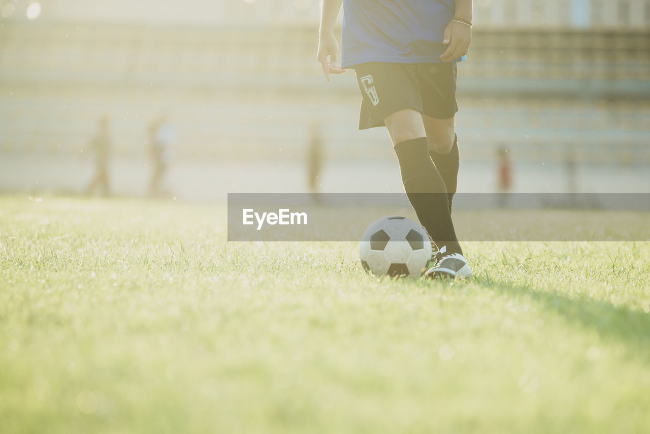 LOW SECTION OF WOMAN PLAYING SOCCER BALL ON GRASS