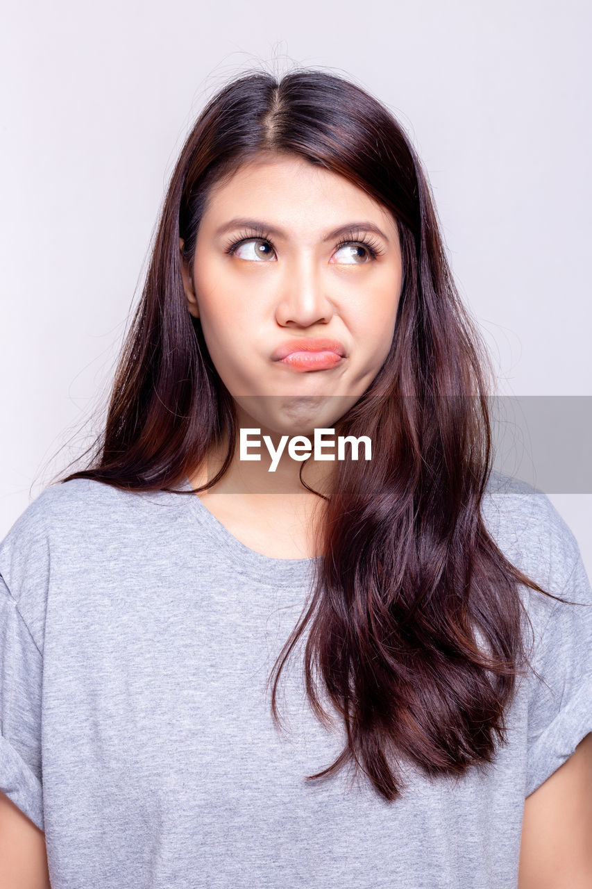 Beautiful young woman making a face against gray background