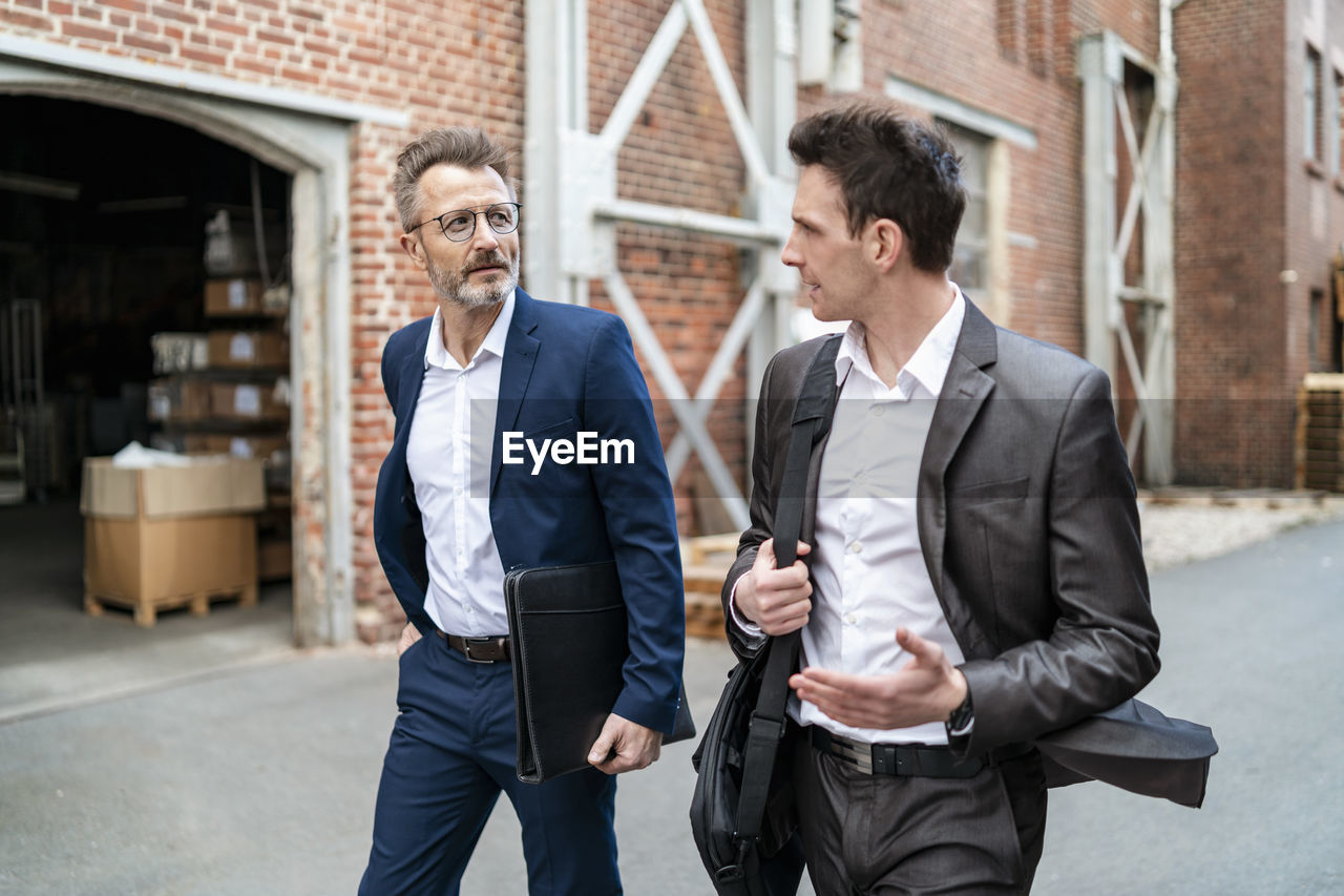 Two businessmen walking and talking at an old brick building