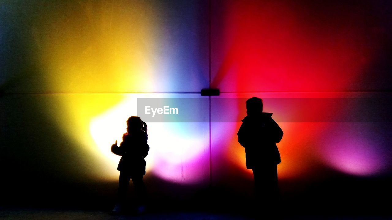 Silhouette people standing against illuminated lights at night