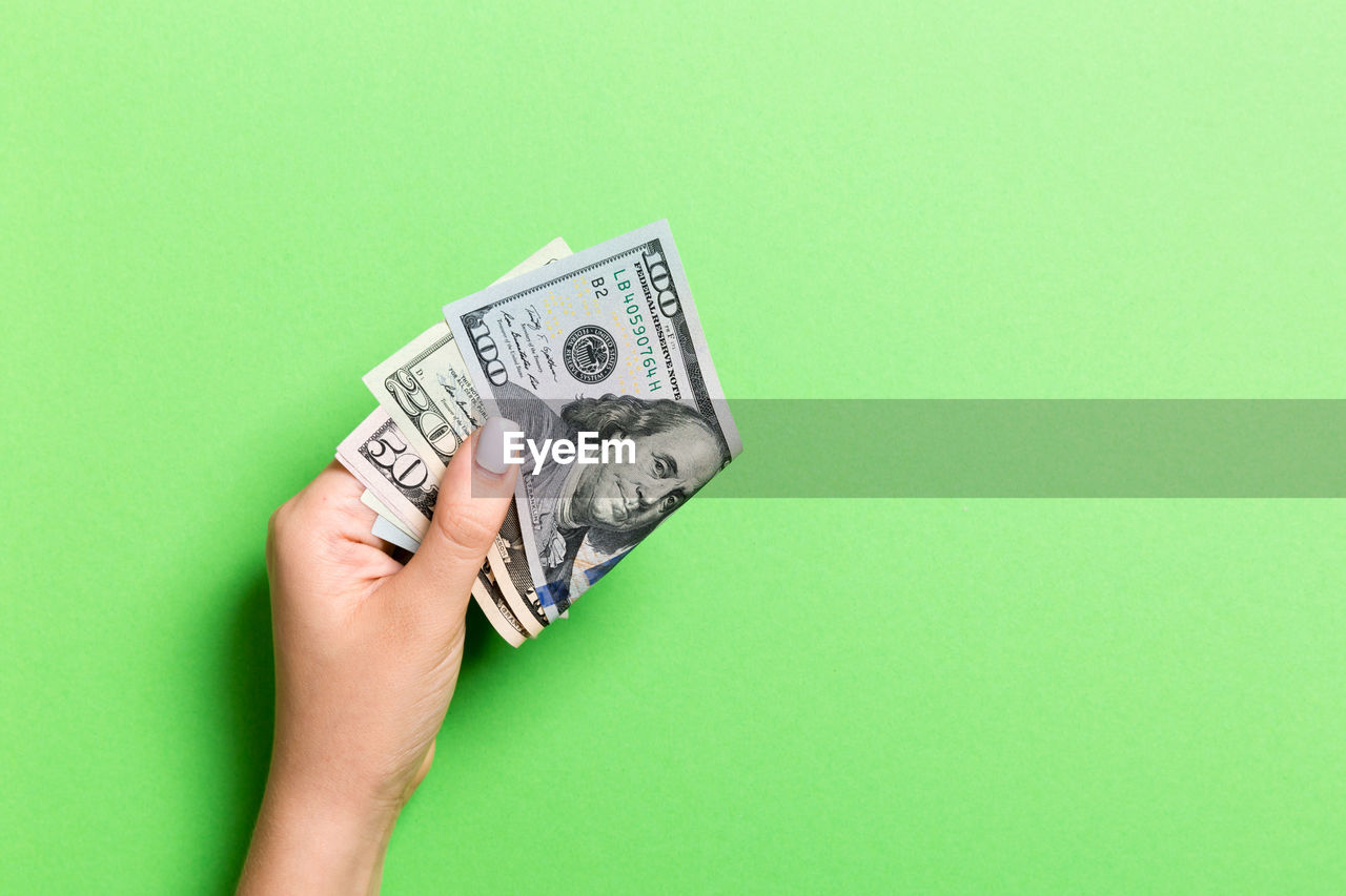 Cropped hand holding paper currency on green background