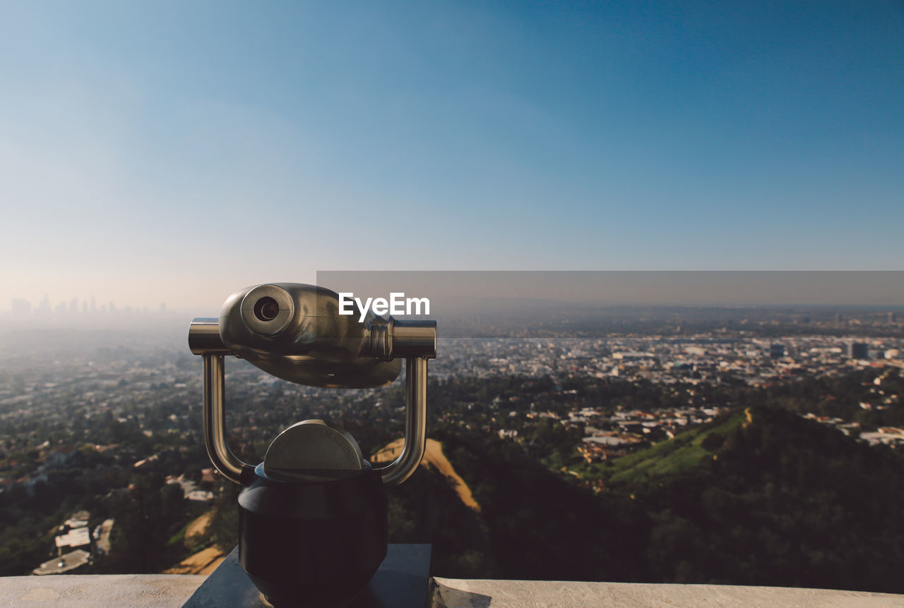 Close-up of coin-operated binoculars on retaining wall over cityscape at griffith point observatory