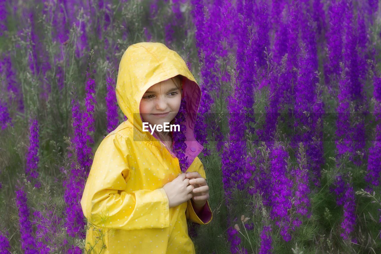 PORTRAIT OF A SMILING GIRL STANDING AGAINST PURPLE FLOWER