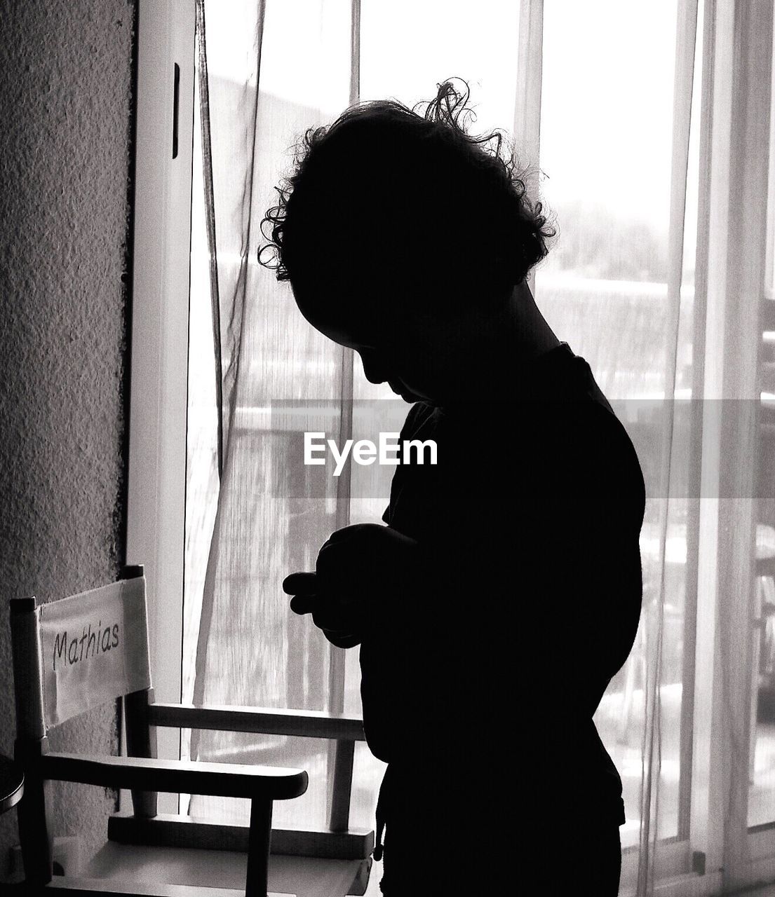 SIDE VIEW OF WOMAN STANDING AGAINST WINDOW AT HOME