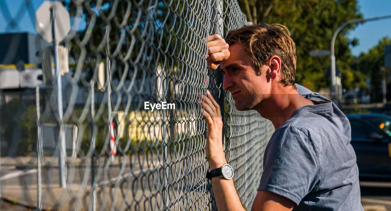 Upset man leaning head against fence. profile view.