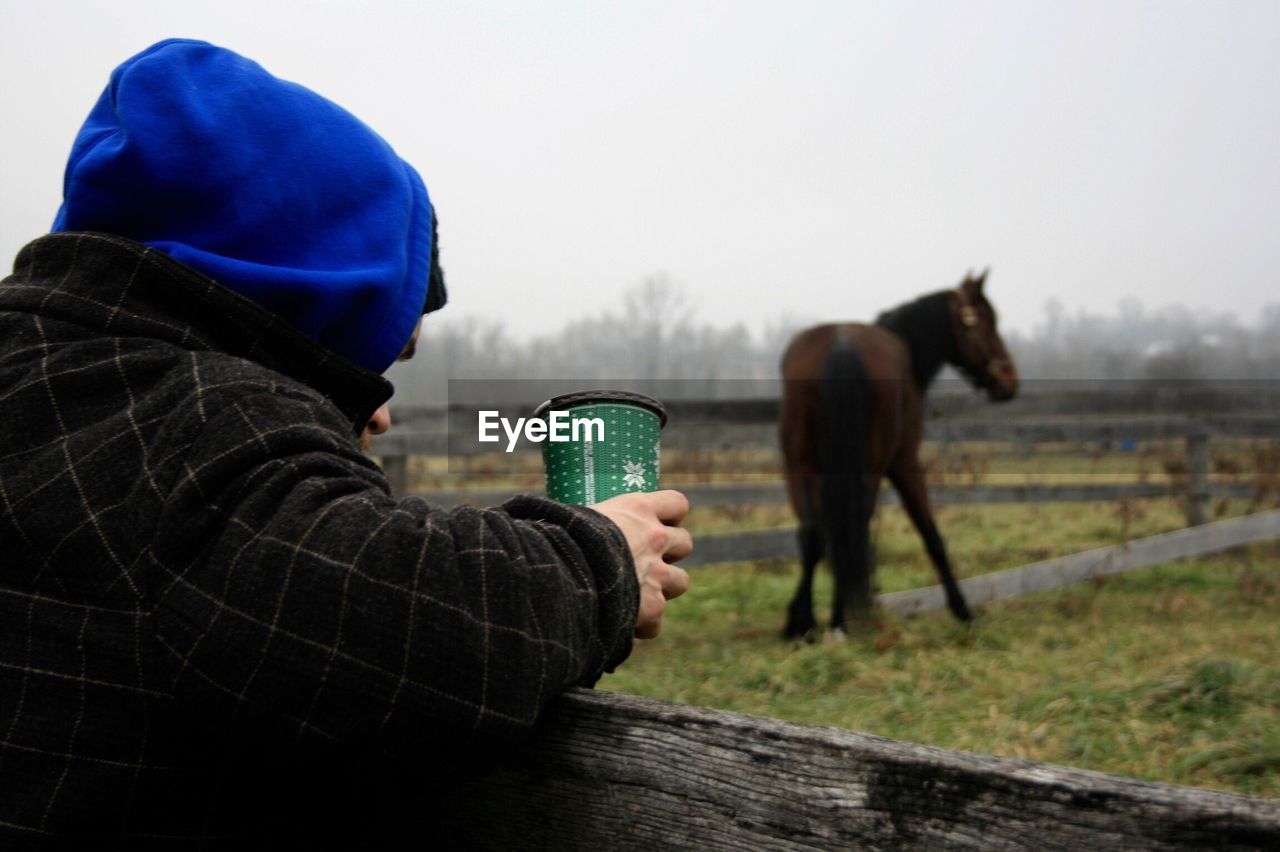 Man holding disposable cup by ranch against horse