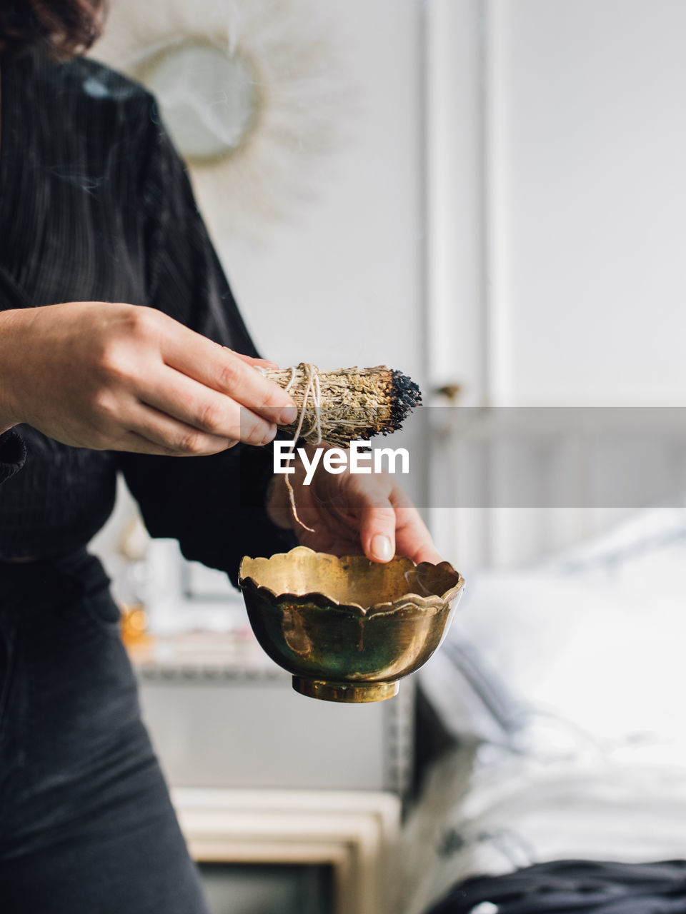 Woman hand holding bundle of sage smudging incense with brass bowl